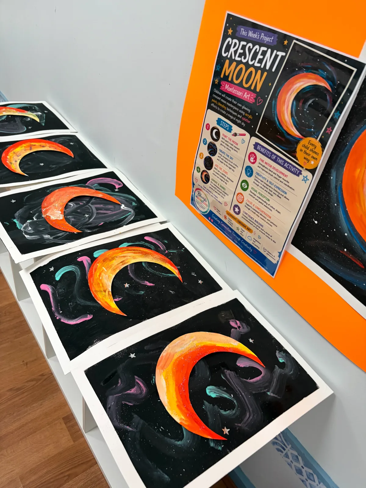 Finished crescent moon paintings lined up after a children's art workshop