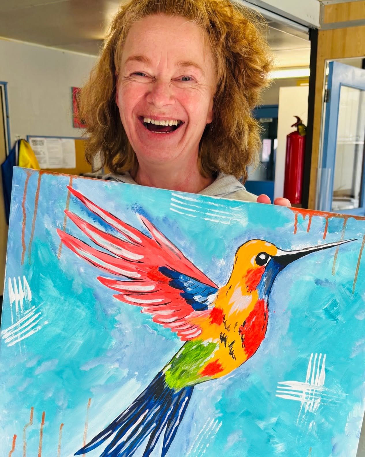 Bluey's Imaginations founder laughing as she holds up her finished hummingbird painting
