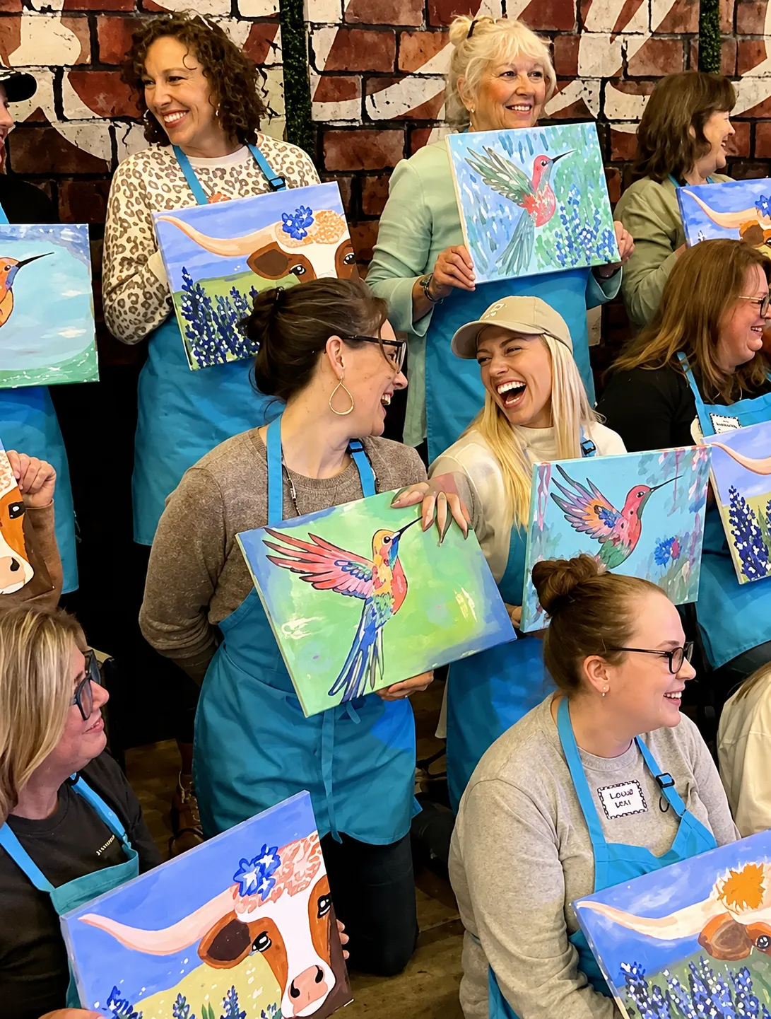 Guests laughing together while holding up the hummingbird and longhorn canvases they painted at a Bluey's Imaginations art class in Endeavour Hills