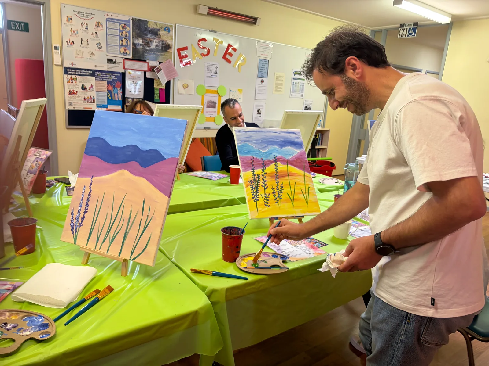 An adult guest painting at an easel during a guided painting session